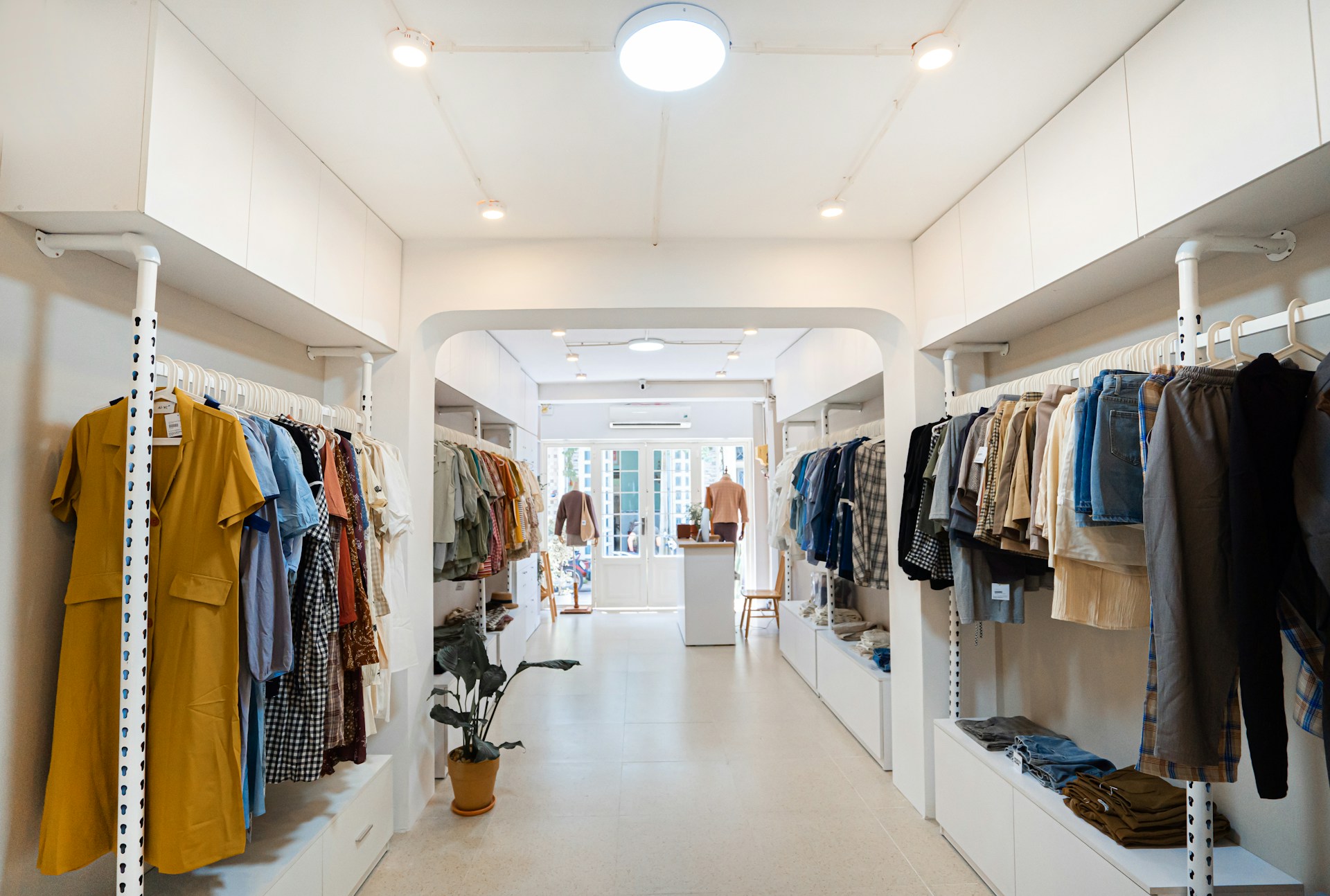 Interior of a modern, minimalist clothing boutique featuring organized racks of apparel, bright lighting, and a welcoming store layout, representing successful retail design.