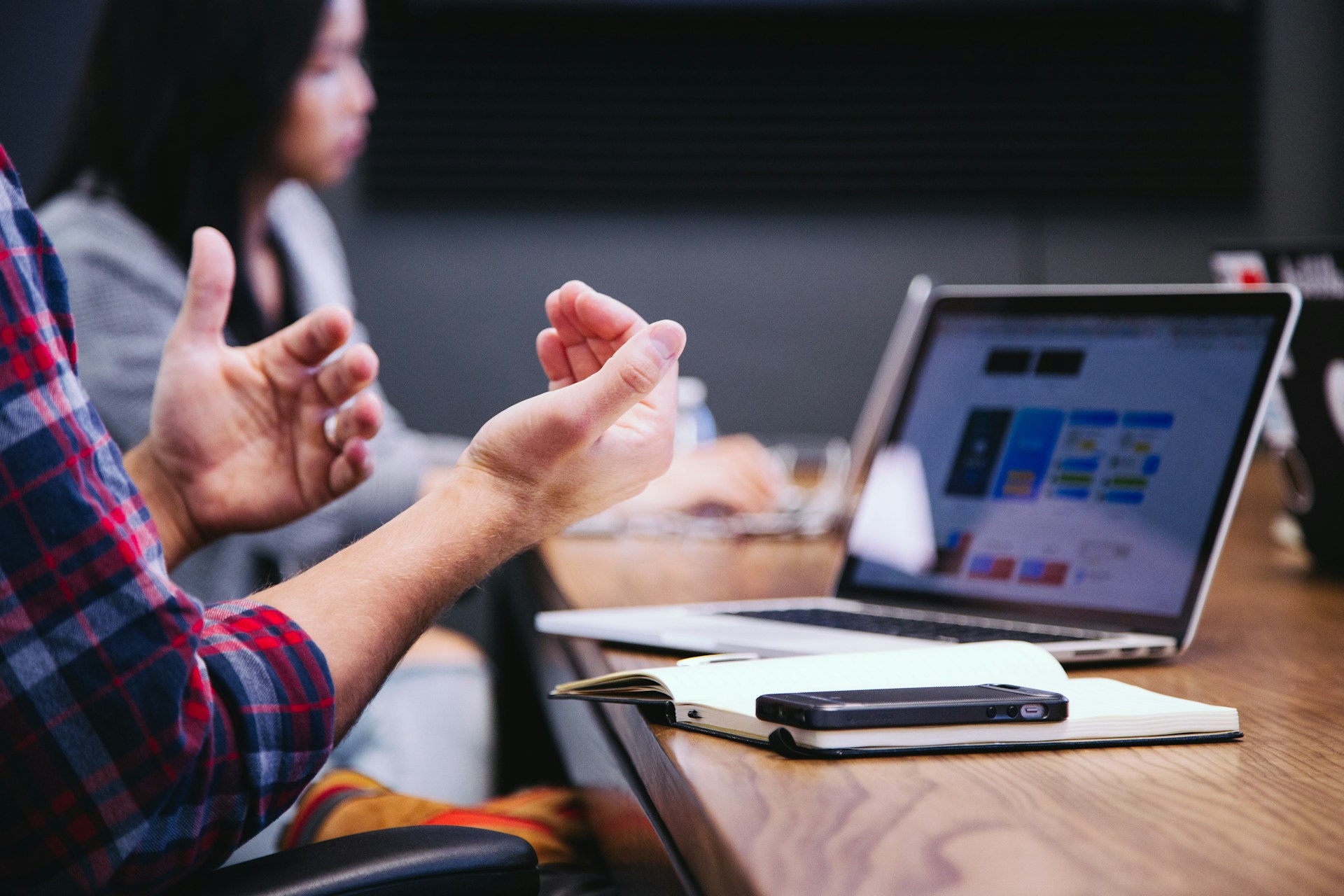 Close-up of a business professional gesturing with hands during a strategic meeting with a laptop and notebook on the conference table.