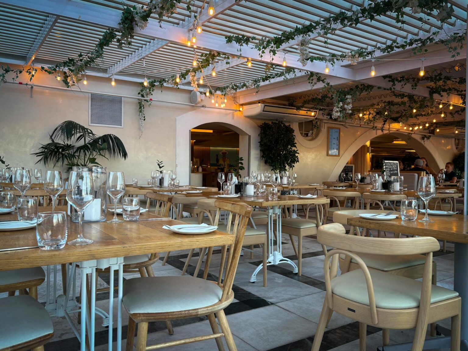Interior of a modern, stylish restaurant with wooden tables set for dinner, hanging string lights, and greenery, representing a ready-to-launch restaurant business.
