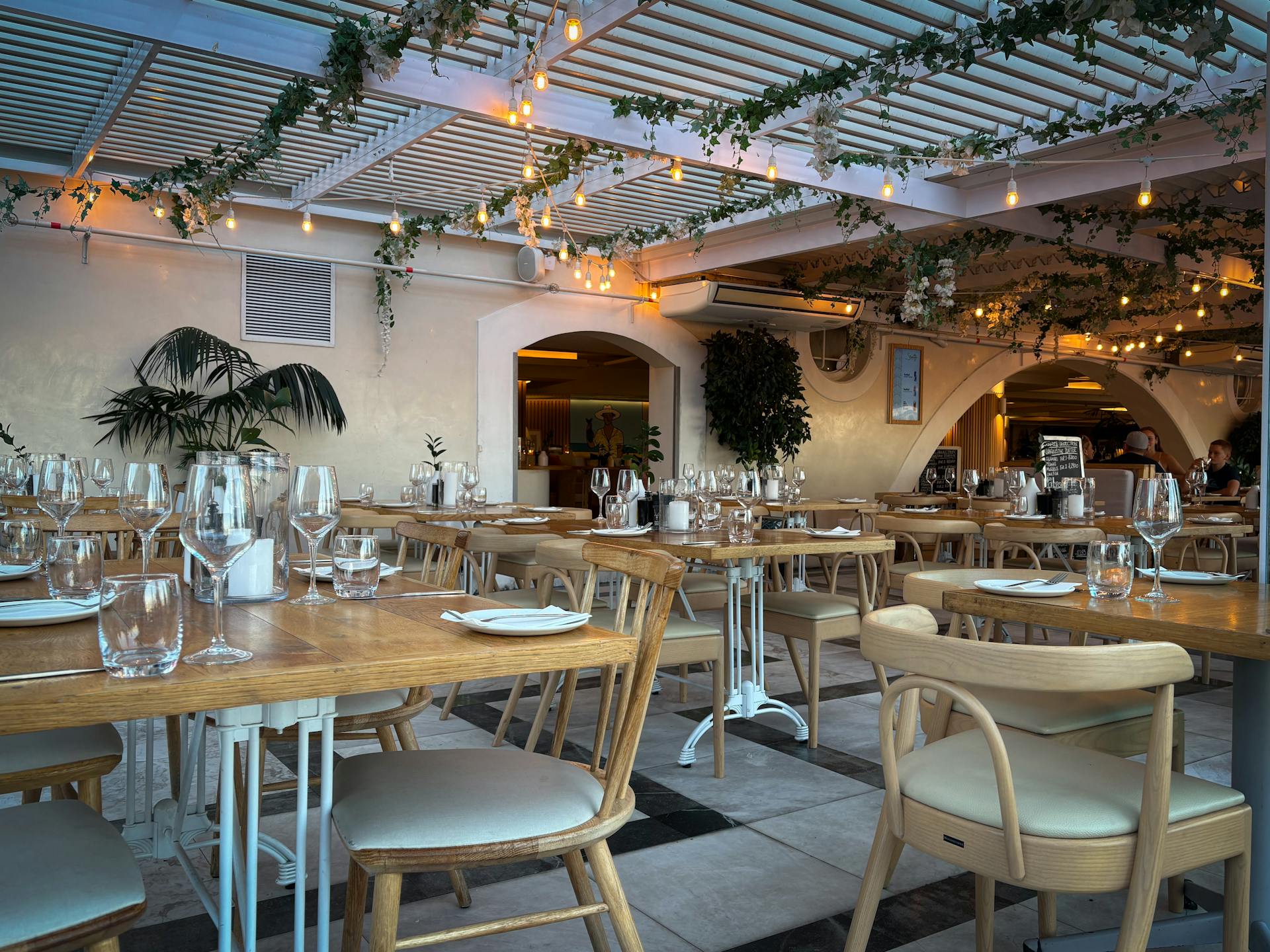 Interior of a modern, stylish restaurant with wooden tables set for dinner, hanging string lights, and greenery, representing a ready-to-launch restaurant business.