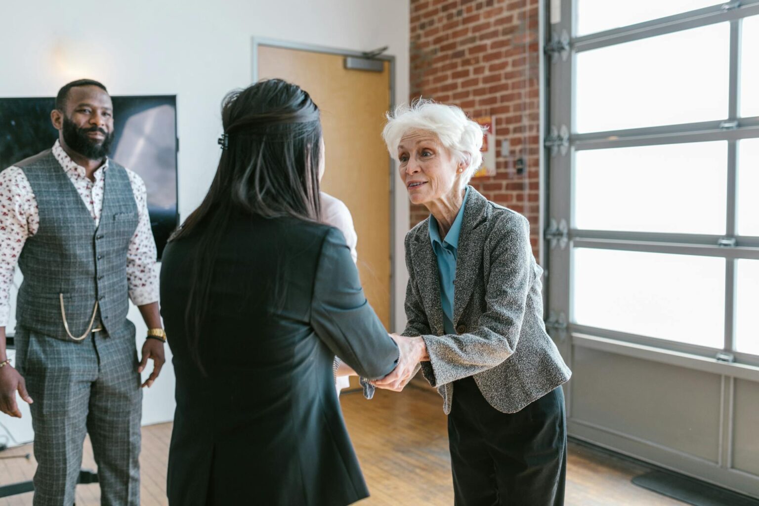 A senior business owner shaking hands with a young entrepreneur in a modern office, representing securing a new client or starting a service-based business partnership.