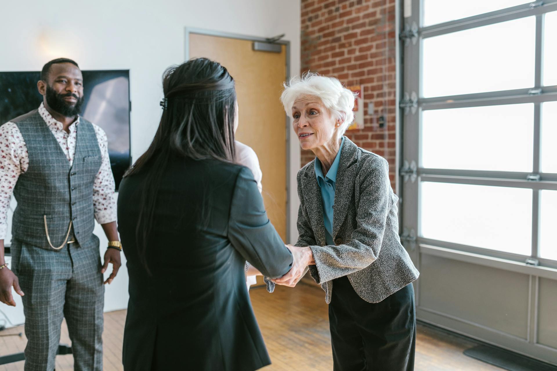 A senior business owner shaking hands with a young entrepreneur in a modern office, representing securing a new client or starting a service-based business partnership.
