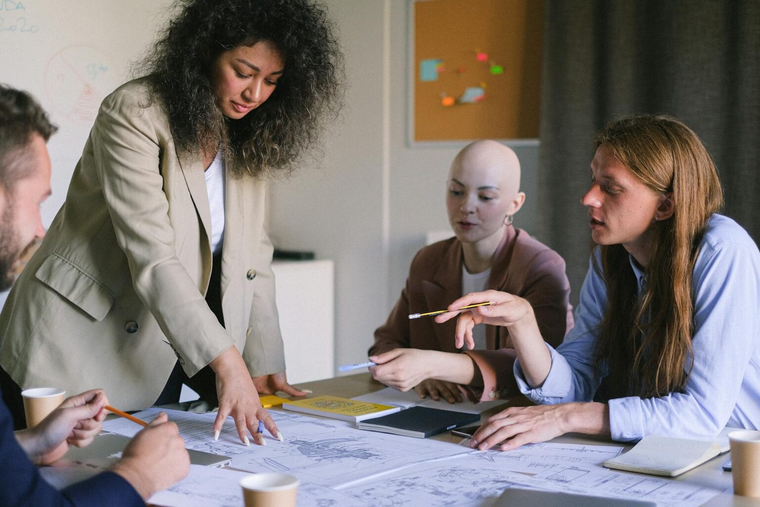 A diverse team of entrepreneurs and professionals brainstorming over business plans and blueprints at a conference table, representing innovation and economic growth.