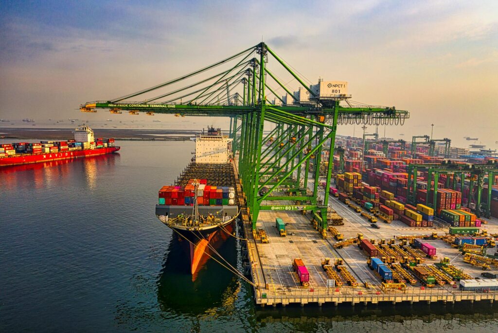 Aerial view of a busy industrial shipping port featuring large green cranes loading colorful cargo containers onto a ship, symbolizing global trade and economic development.